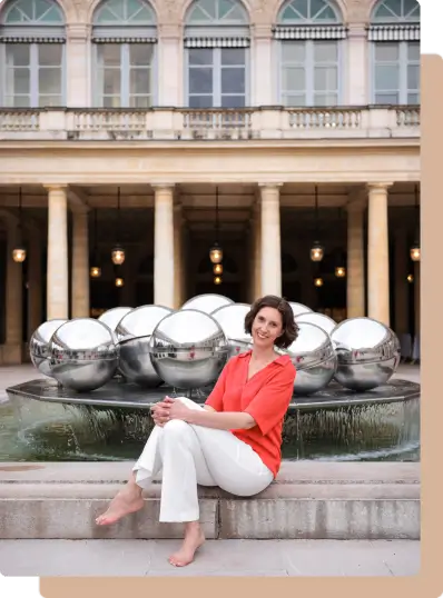 Muriel Joubert assise devant une fontaine les jambes croisées et pieds nus.