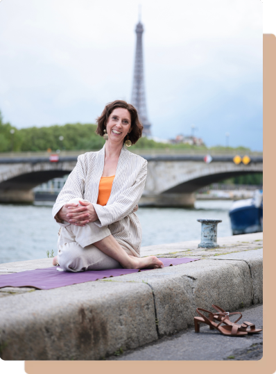 Muriel Joubert assise en posture de Yoga dehors sur un tapis avec la Tour Eifel derrière elle.