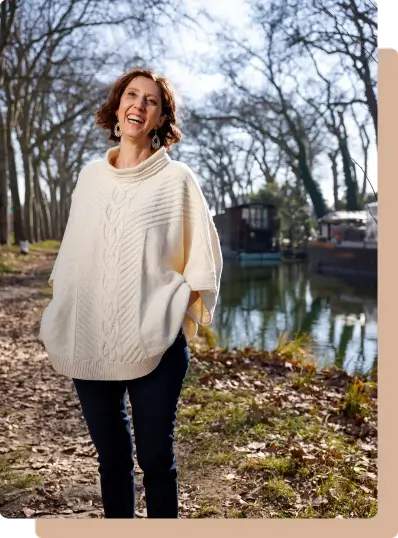 Muriel Joubert portant un pull en automne souriante devant une rivière.